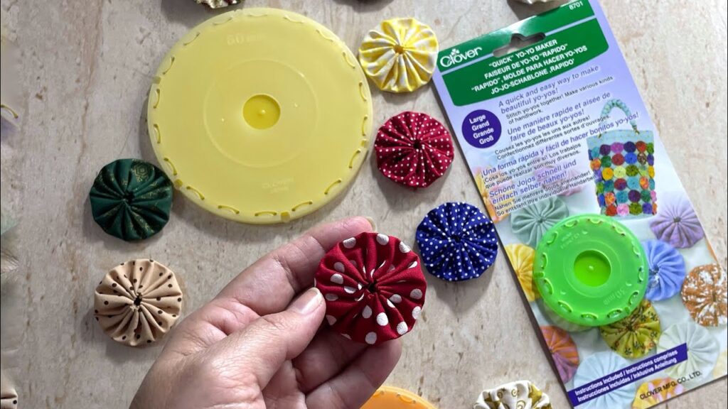 Herramientas "Quick Yo-Yo Maker" de la marca Clover junto a varios yo-yos de tela de colores con estampados de lunares y flores.