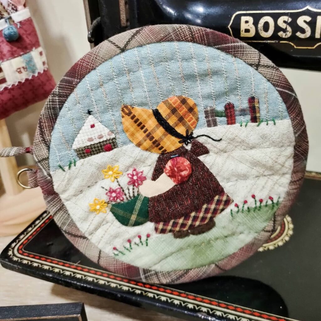 Labor de patchwork circular con diseño de una niña con sombrero en un paisaje rural.