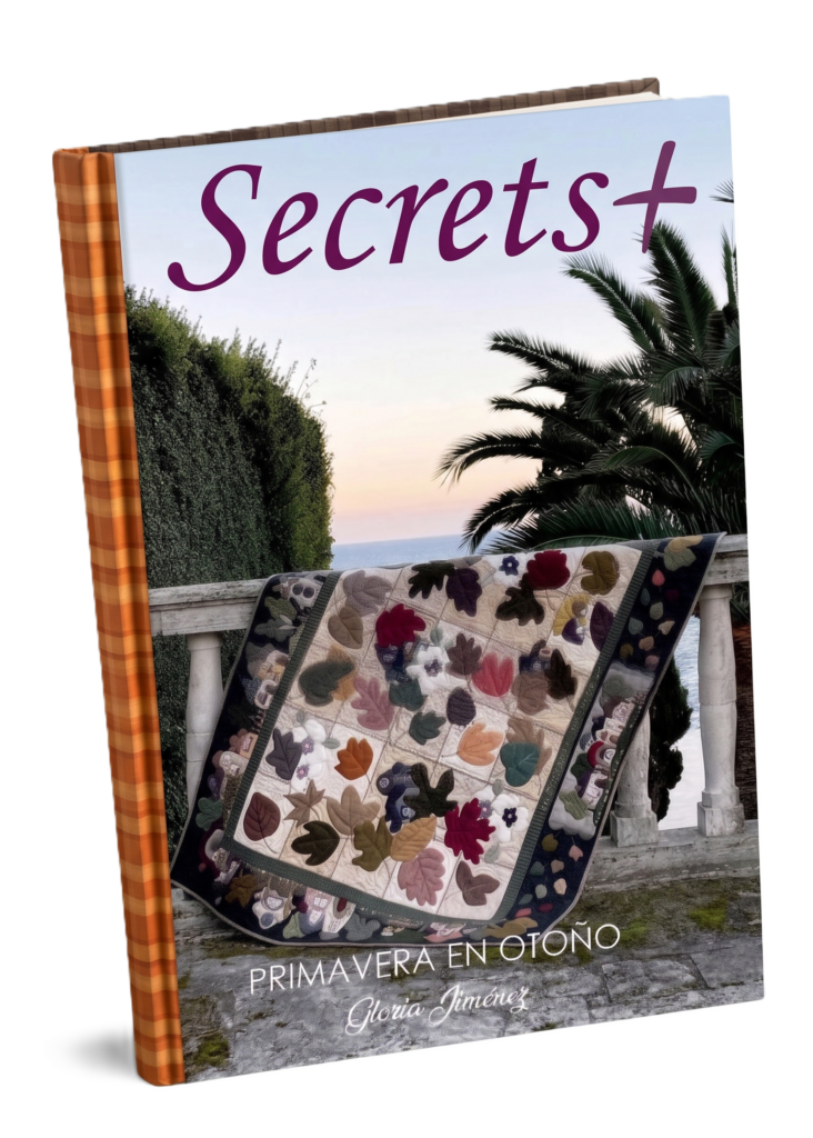 Libro de patchwork titulado "Secrets" que muestra una colcha con diseños florales en un entorno exterior.