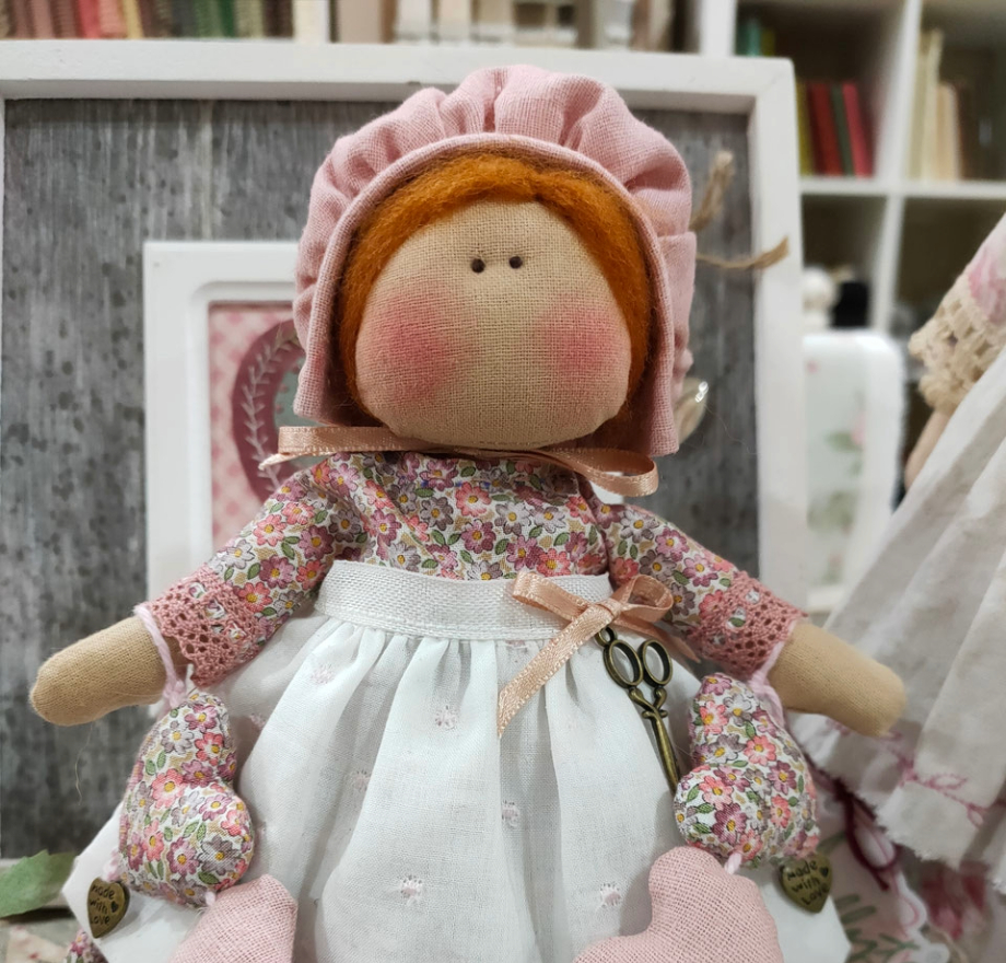 Muñeca de trapo artesanal con vestido de flores, delantal blanco y gorro rosa, hecha a mano con técnicas de costura creativa.